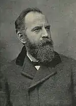 A man with an overcoat looks to the right of the viewer; he has a full beard