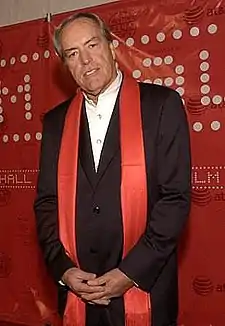 A color photograph of a man wearing a black and white suit with a red scarf hanging around his neck