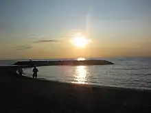 The sun setting over a darkened beach and breakwater.