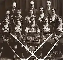 Black and white photo of hockey players wearing uniforms and equipment seated in two rows on benches