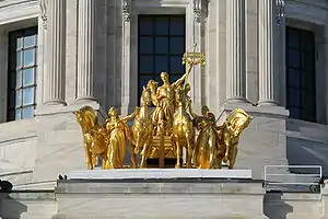 Golden statue of man on a chariot with two women leading the horses