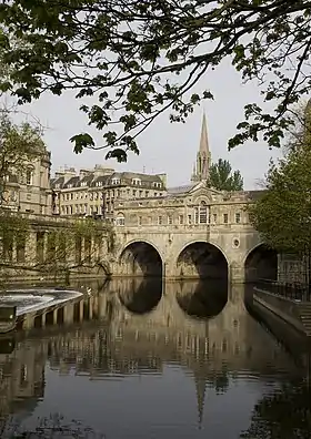 Water in the foreground reflecting an arched bridge of honey-coloured stone.