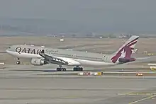 A white A330 over land, marked with Qatar Airways and its logo on the vertical stabiliser, gear extended