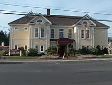 A picture of the old school house, a yellow building with white trim.