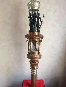 Colour photograph of an elaborate ceremonial staff with bronze and silver elements including a crown held up by a group of Gurkha soldiers.