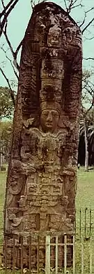 A tall, narrow monument with the prominent sculpture of a king surrounded by elaborate decoration