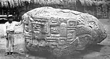 A man standing beside a large sculptured boulder