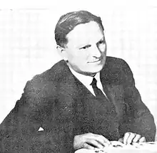 black and white photo of a seated man whose hands are on a book