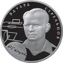 A silver coin with Strelstov's head and neck illustrated in relief upon it, accompanied by the outlines of a football pitch and a football and his name in Russian.