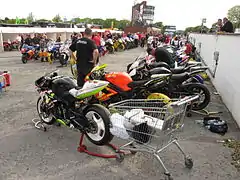 Pre-race assembly area adjacent to startline showing machines with tyre warmers plugged into wall-mounted electrical outlets