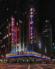 A building in a city at night that reads "RADIO CITY" in all caps lit up in various places around the building