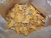 Raisins and bran flakes, inside a cereal box.  Multiple raisins are visible on top of the flakes