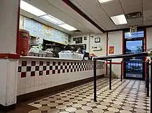 Photograph of a restaurant interior with a counter, black and white tiling, and a menu display