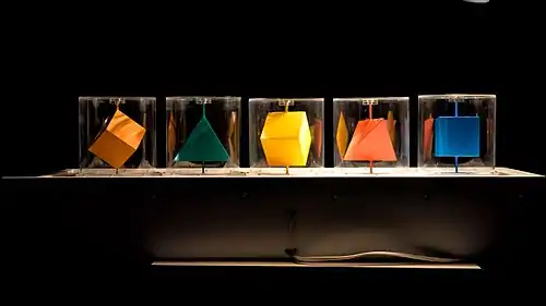 five coloured polyhedra mounted on vertical axes