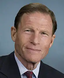 A white man in a suit and red tie.