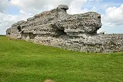 A grey wall, several metres tall, with grass in front.