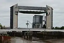 Two concrete towers over a river, linked with a span across their tops and a green barrier in a horizontal position