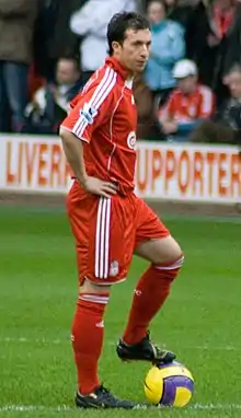 A man dressed all in red standing with his hands on his hips and his left foot on a yellow ball