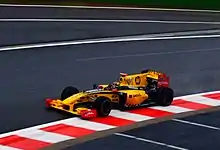 A yellow and black Formula One vehicle being driven uphill on a race circuit