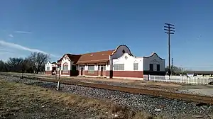 A building which is 195 feet (59 m) long and 26 feet (7.9 m) wide. The building architecture is eclectic, exhibiting both Spanish and Italian influences. The lower section of the exterior wall is brick, while there is covered with stucco. The stucco is painted white, decorated with tan painted trim. The center section has a gabled roof, with semicircular walls extending above the roof line on each end. The large window in the center is arched. Other windows have an arch design embedded in the stucco.