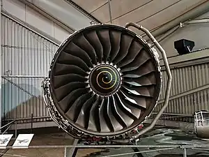 Rolls-Royce Trent 900 116 inch diameter fan. The fan has supersonic relative velocities in the outer half which result in shock waves in the passages. Visually evident are the blade leading edge sweep which changes from hub to tip from forward to backward to forward and the blade twist which varies from  almost axial at the hub to almost circumferential at the tip. The shape of the blade positions the shock far enough behind the leading edge to prevent expulsion of the shockwave beyond the tip leading edge (prevents surge and flutter). Each radial section with its contribution to leading edge sweep and blade twist has its centrifugal force acting close to a radial line which minimizes stress due to rotation.