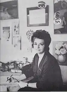 Rosa Rosenberg at her some studio in Mexico City, she is holding pens and brushes, and some of her artwork is visible in the background.