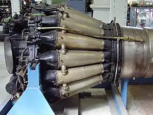 de Havilland Goblin with sixteen straight-through combustion chambers. Each consists of a flame tube enclosed in a pressure-tight outer casing. They are connected by tubes which balance the pressure and propagate the flame during start from the two tubes with igniters one of which is shown on a top tube.