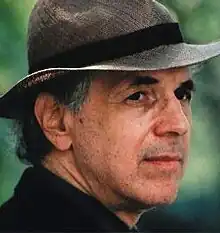 Man with greying hair and designer stubble, wearing a hat with a brim