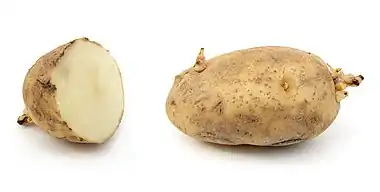 A sliced and a whole potato side by side, both dark brown with sprouts emerging.