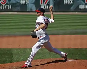 A man in a white baseball uniform pitches a ball from the mound