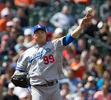 A Korean man wearing a grey Los Angeles baseball uniform Throwing a ball.