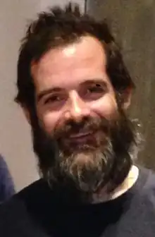 A smiling man with brown hair and a thick beard