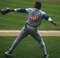 A man wearing a blue hat and gray baseball uniform bearing the number 21 prepares to throw a baseball.