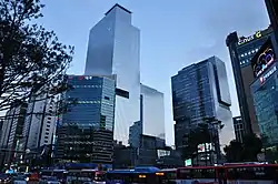 Several modern blue glass skyscrapers are visible. It is the early evening and a row of buses can be seen at the bottom of the photograph.