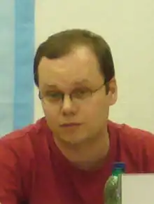 Saša Gedeon wearing glasses and red t-shirt, looking at camera