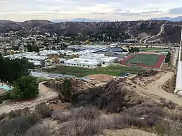 Elevated view of a cluster of low, white rectangular buildings with a line of hills in the near background.