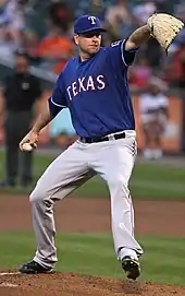 Pitcher in blue baseball cap coming out of his windup as he delivers a pitch to the plate