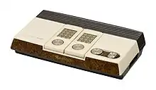 Gray rectangular console with two controllers. Controllers have number pads and circular dials