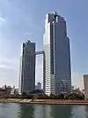 Ground-level view of two blueish-grey buildings connected by an enclosed corridor near the top of the buildings