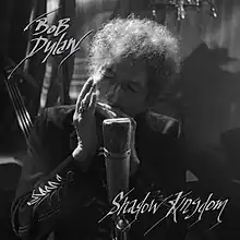 A black-and-white photo of Dylan playing harmonica into a microphone