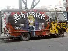 A portrait of a woman dressed in a white crop top and blue pants is painted on a colourful van. The word "Shakira" is written in white behind her.