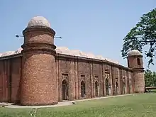 Building of red bricks with a roof consisting of many white domes. There are small round towers on the corners of the building each crowned by a white cupola.