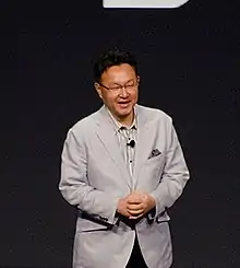 Shuhei Yoshida speaking on a stage.