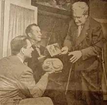 Three men demonstrate the Aztec hoax claims using an inverted bowl to represent Earth and a copy of Frank Scully's book to represent a magnetism-powered flying saucer.