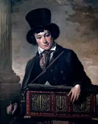 Very young white man, clean-shaven, wearing a top hat and carrying a portable barrel organ