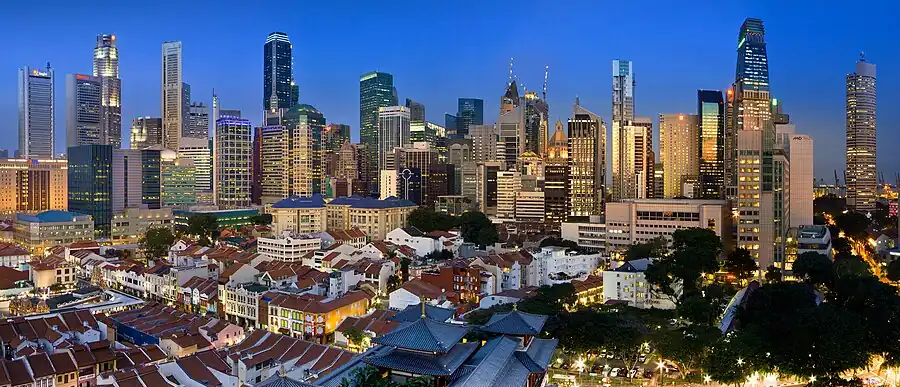 Skyline of a city, showing several tall skyscrapers. The tallest buildings are at the left and right of the image, with several low-rises in the immediate foreground. Most of the towers are lit up, as night is approaching