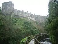 A two- and three-storey building on top of an escarpment. Below the escarpment is a fenced footpath curving away from the photographer's perspective to the right.