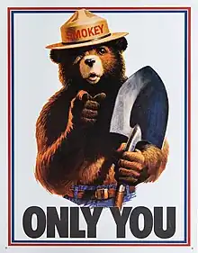 Drawing of a grizzly bear with human features. He is wearing blue jeans with a belt and a brimmed hat with the name "Smokey" on the cap and has a shovel in his left hand. He is pointing to the viewer while the text "Only You" is seen below him.