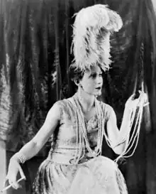 Young white woman in elaborate 1920s evening costume, with copious pearl necklace and holding a cigarette in a long holder