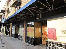 Photograph of the exterior of a two-story brick building with boarded windows and graffiti